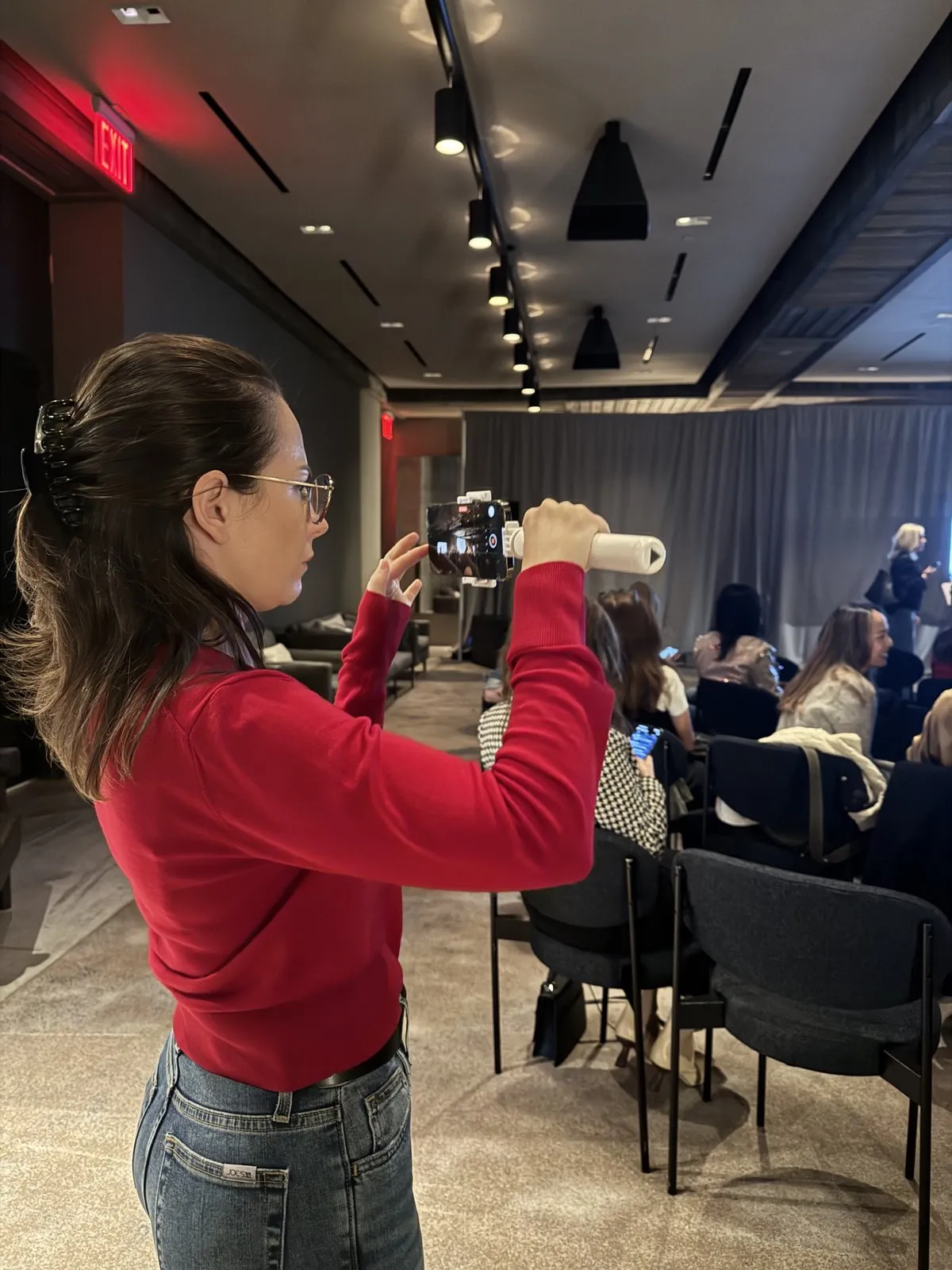 Our founder filming a conference session on her phone, with attendees seated behind her