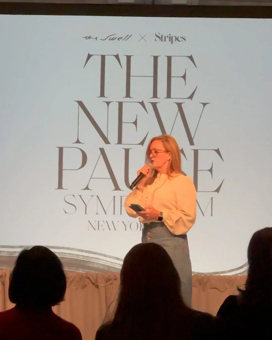 A speaker on a stage in front of a large backdrop, with the audience seated in the foreground