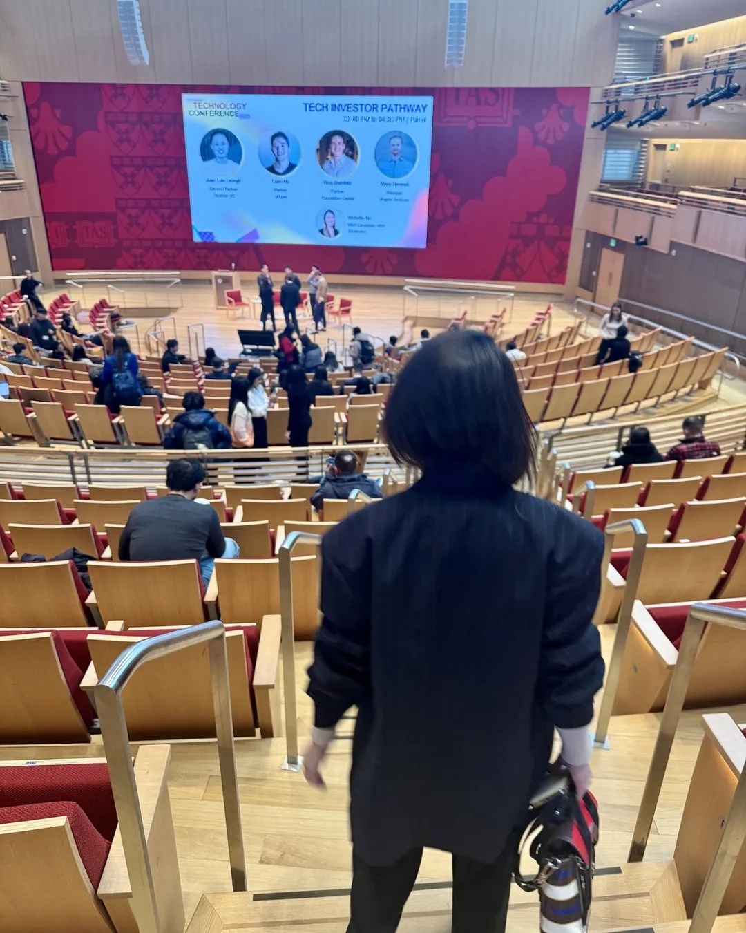 A large tiered auditorium with attendees seated, facing a stage and a big screen