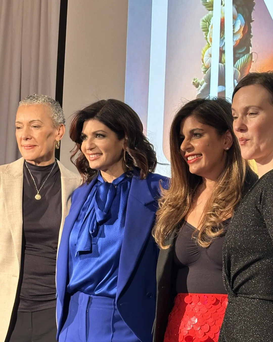 Four women posing together at an event, one of them in a bright blue suit