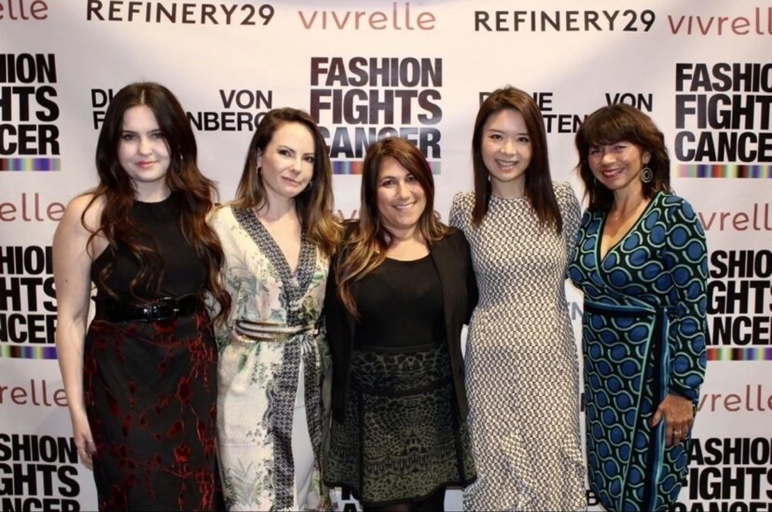 Five women posing together in front of a Fashion Fights Cancer press wall