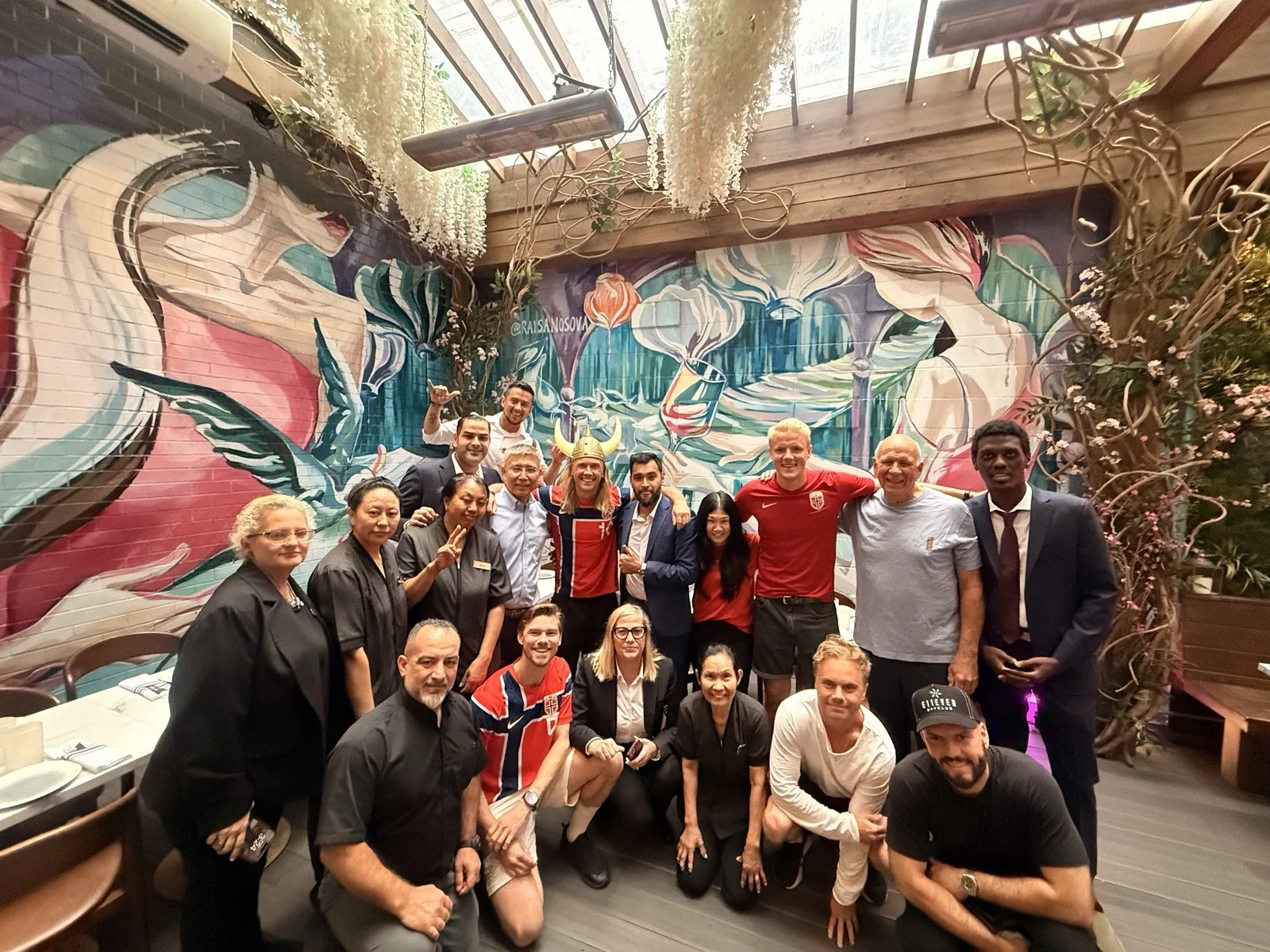 A large group of people posing together on a terrace in front of a colorful mural