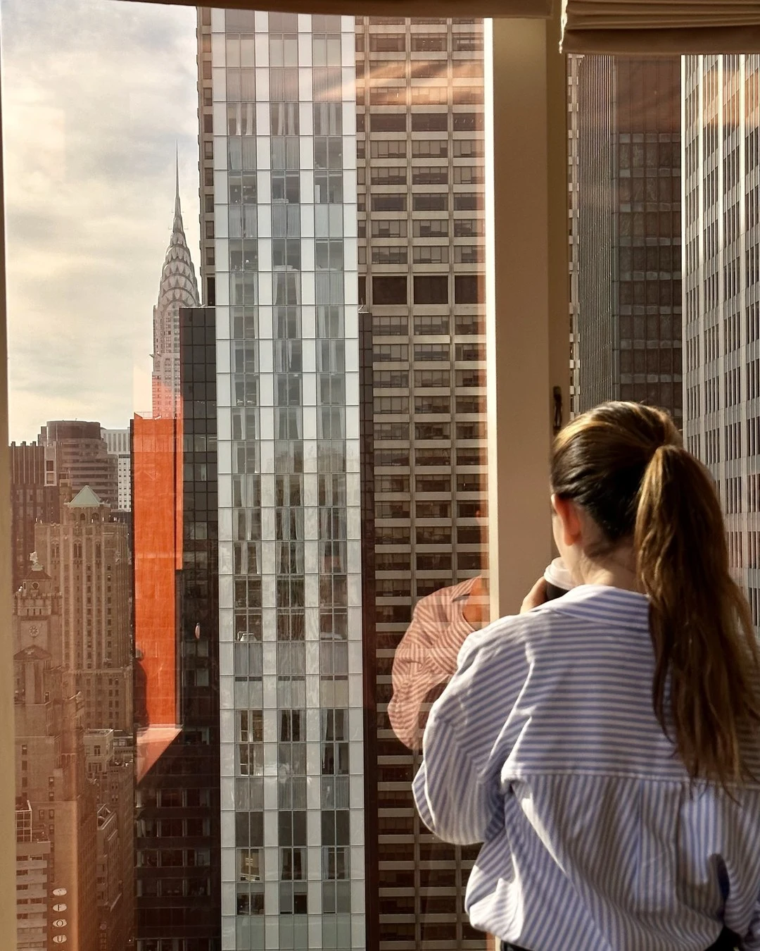 A woman looking out of a high window at the Chrysler Building and neighboring towers